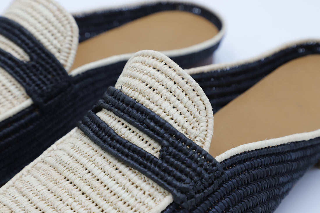Close-up of a sandal with black woven straps and beige sole on a white background