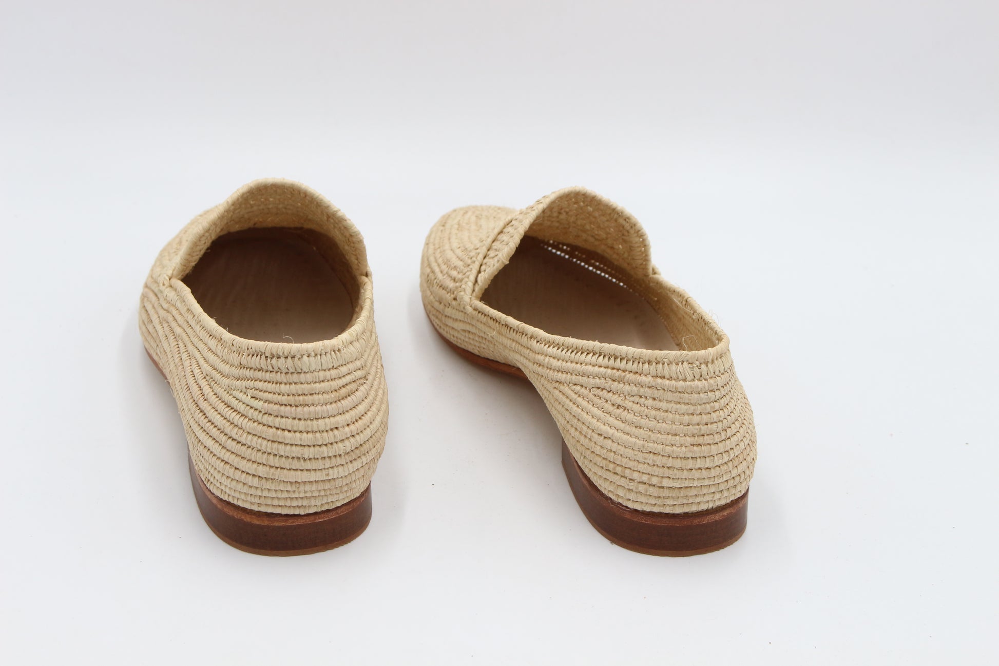 Pair of beige woven shoes with brown soles on a white background