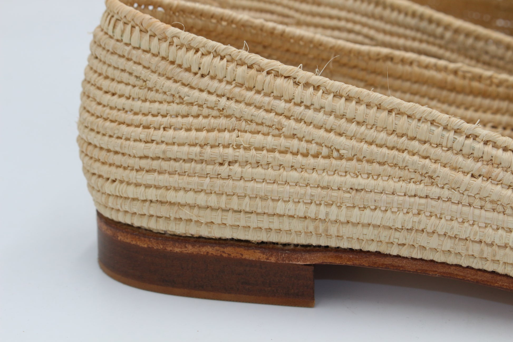 Close-up of a woven beige flat shoe with a brown sole on a light gray background